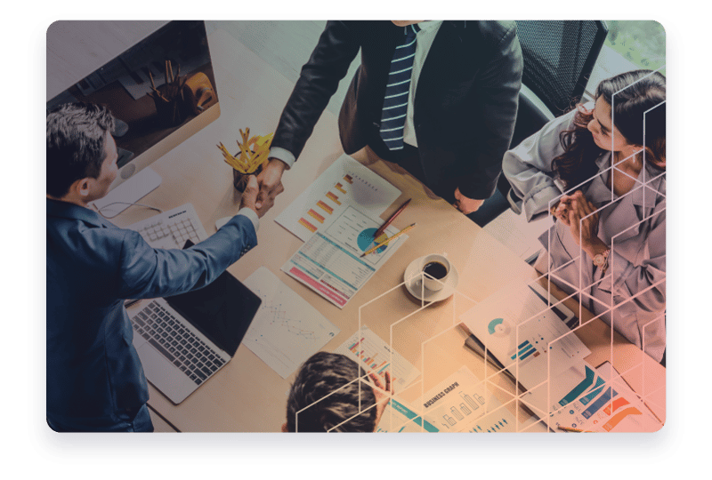 A group of business individuals shaking and with charts on the table.